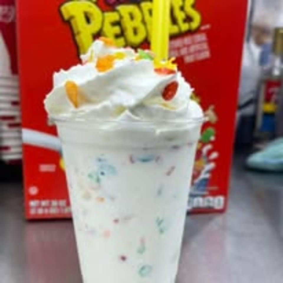 A Route 10 Drive-In milkshake with whipped cream and colorful cereal, with a red cereal box in the background.