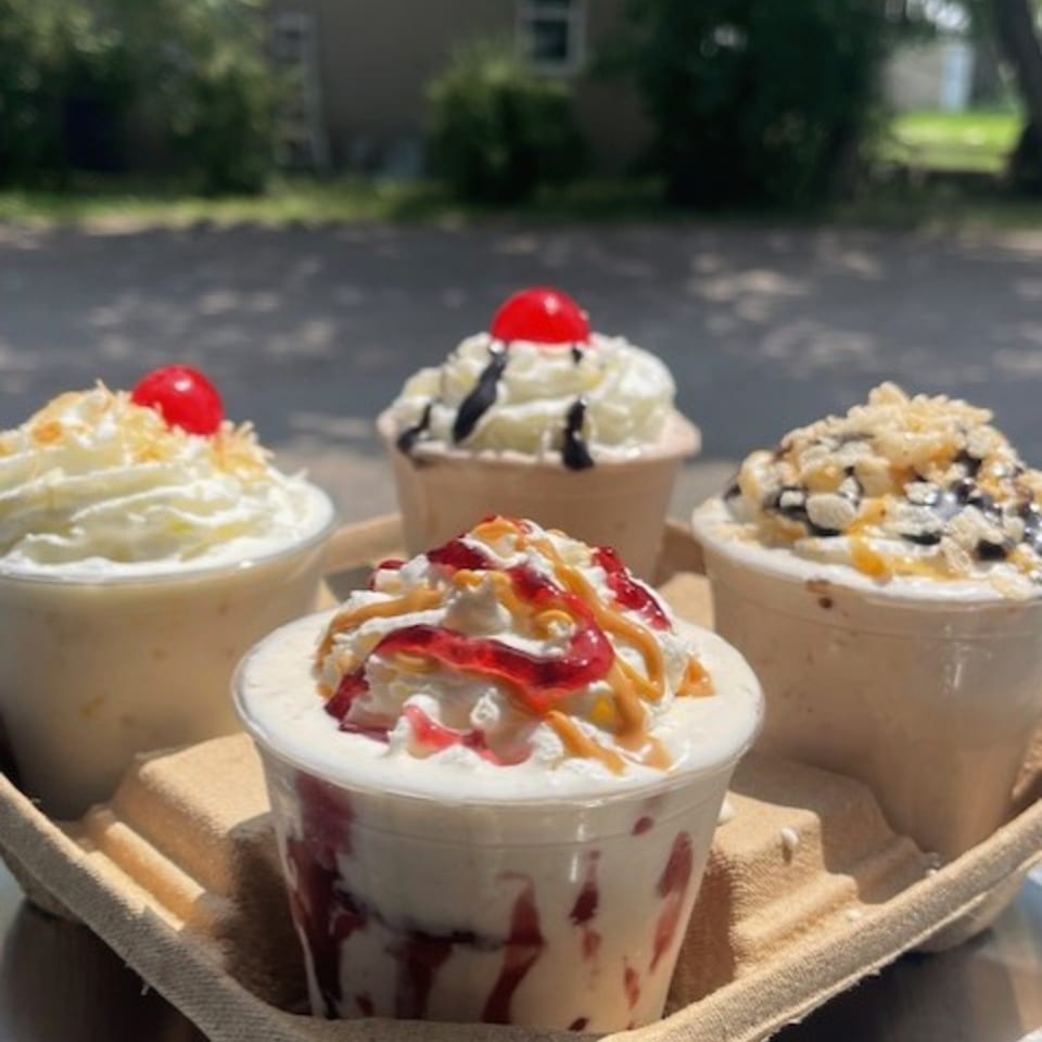 Four Route 10 Drive-In milkshakes with whipped cream, cherries, and various toppings in a carrier.