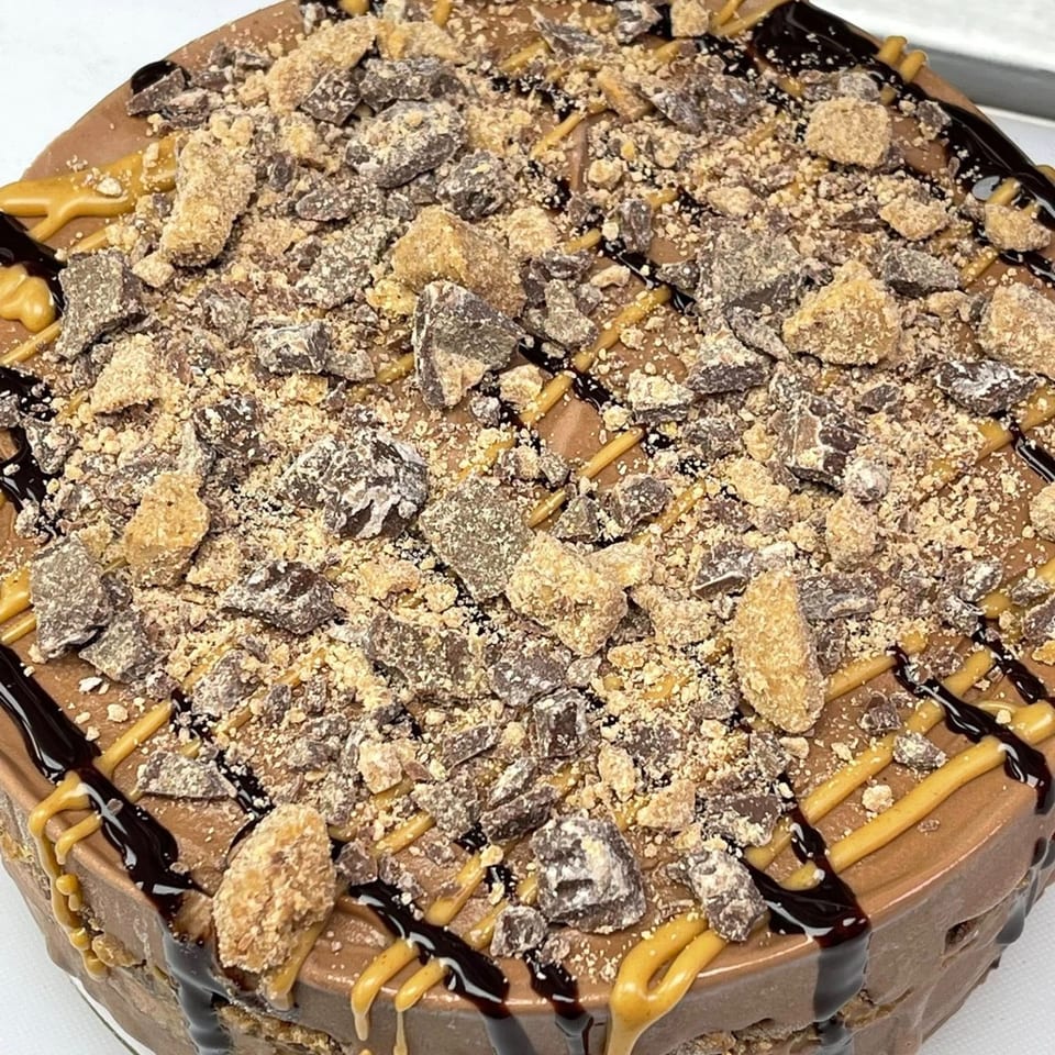 A chocolate ice cream cake topped with crushed candy, chocolate drizzle, and peanut butter sauce.