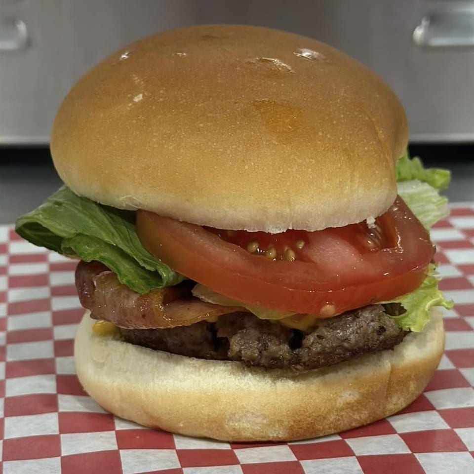 A Route 10 Drive-In bacon cheeseburger with lettuce and tomato on a red and white checkered paper.